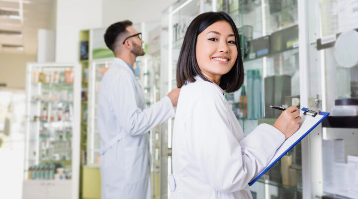 Happy pharmacist in white coat writing on clipboard