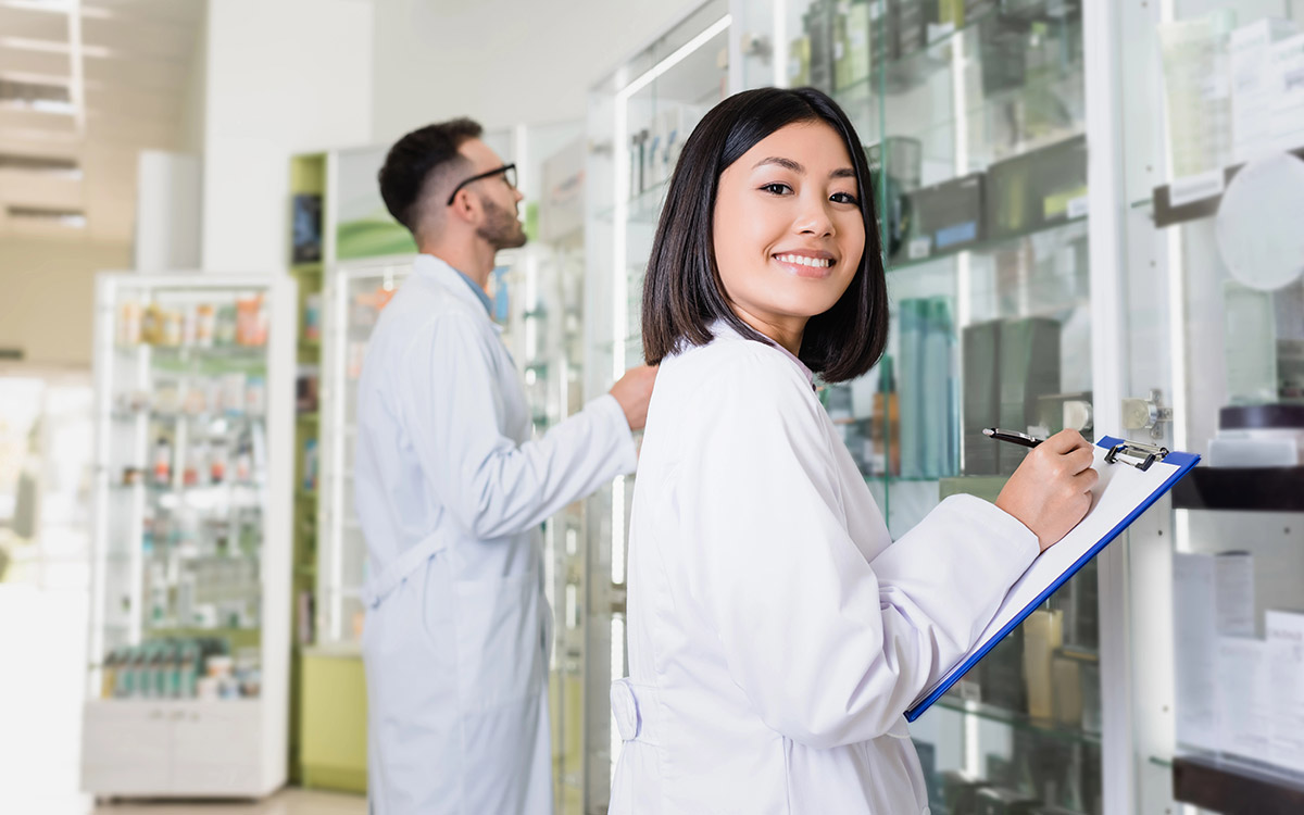 Happy pharmacist in white coat writing on clipboard