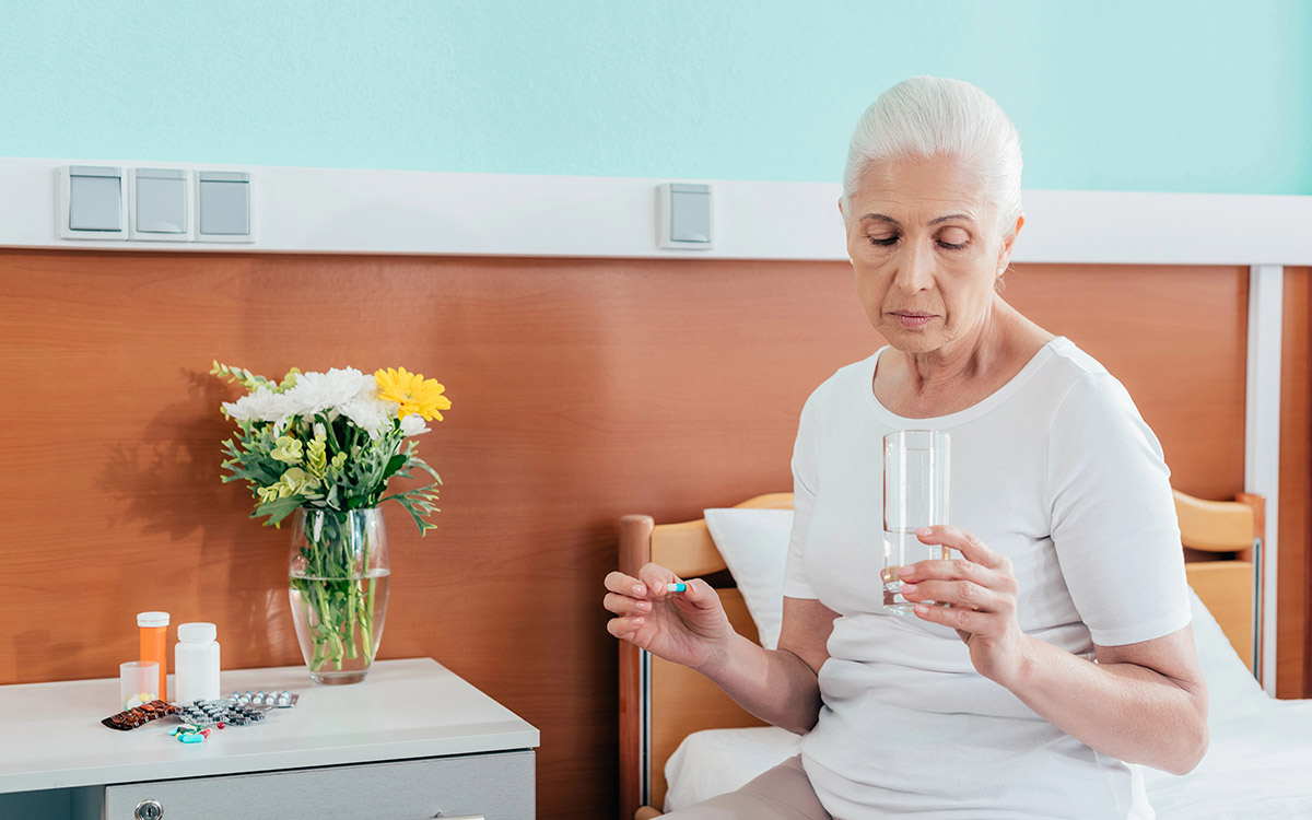 Senior woman taking medicine next to her bed
