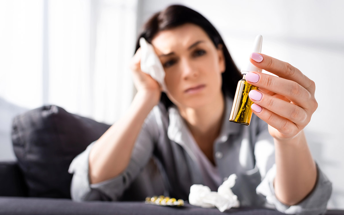 woman with nasal sparay in hand not feeling well
