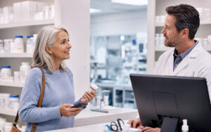 Older woman discussing a prescription transfer with a pharmacist at a modern compounding pharmacy counter