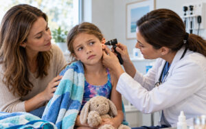 Pediatric doctor examining a child's ear for infection while her mother offers comfort